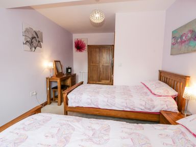 A bedroom with two single beds wooden furniture a wardrobe and floral pictures at 6 Stad Yr Ysgol in Manod near Blaenau Ffestiniog