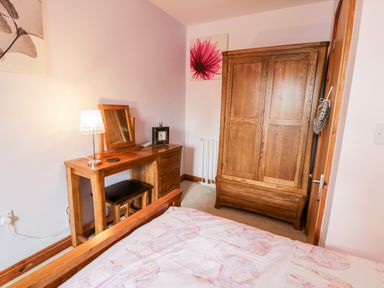 A bedroom with a wooden dressing table lamp mirror chair wooden wardrobe and bed at 6 Stad Yr Ysgol in Manod near Blaenau Ffestiniog
