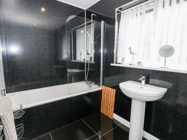 A bathroom with a bathtub and shower, a pedestal sink, a window with vertical blinds, and black speckled walls at 6 Stad Yr Ysgol Manod near Blaenau Ffestiniog