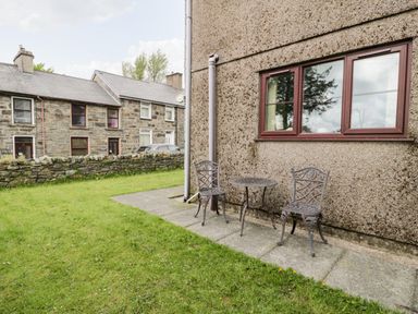 An outdoor space with two metal chairs and a small round table next to a building with a pebble exterior wall and a window at 6 Stad Yr Ysgol in Manod near Blaenau Ffestiniog