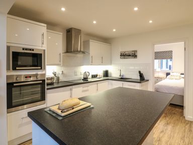 A kitchen with black countertops white cabinets and a loaf of bread on a cutting board at Keepers Cottage in Sidmouth