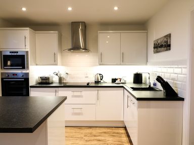 A kitchen with white cabinets black countertops a stainless steel oven microwave toaster kettle knife block and a black sink at Keepers Cottage in Sidmouth