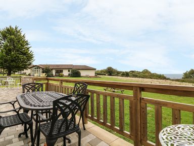 An outdoor patio area with black metal table and chairs a wooden fence and grassy field at Keepers Cottage in Sidmouth