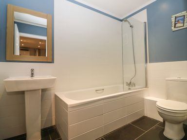 A bathroom with a sink and mirror bathtub with shower and toilet at Keepers Cottage in Sidmouth
