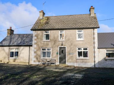 The front exterior of a two story stone cottage with a bench and a door at Rosies Cottage in Bushmills County Antrim