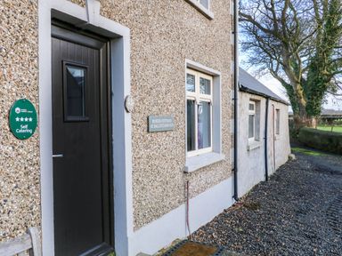 The exterior of Rosies Cottage with a black door a window a green self catering sign and a gravel path at Rosies Cottage in Bushmills County Antrim