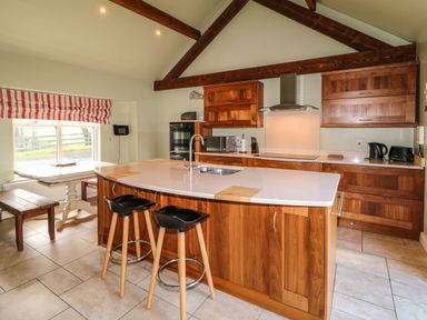 A kitchen with wooden cabinets an island with stools and a dining table by a window at Rosies Cottage in Bushmills County Antrim