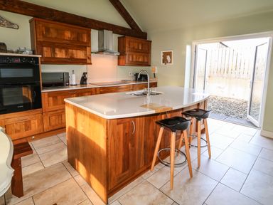 A kitchen with wooden cabinets a central island with a sink two stools and open patio doors at Rosies Cottage in Bushmills County Antrim