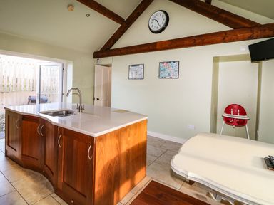 A kitchen with a wooden island countertop a wall clock two framed pictures a red high chair and a white table at Rosies Cottage in Bushmills County Antrim