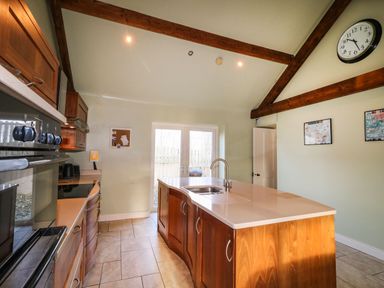 A kitchen with a central island and wooden cabinets under exposed wooden beams at Rosies Cottage in Bushmills County Antrim