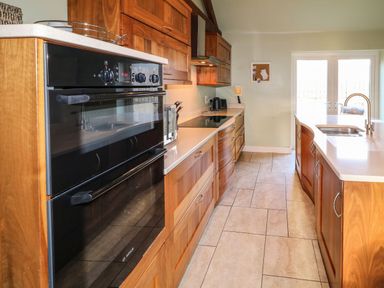 A kitchen with wooden cabinets a double oven a stovetop a sink and double glass doors at Rosies Cottage in Bushmills County Antrim