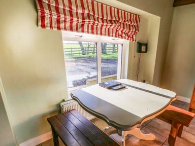 A dining area with a white table, wooden benches, and a window with red and white striped blinds at Rosies Cottage in Bushmills County Antrim