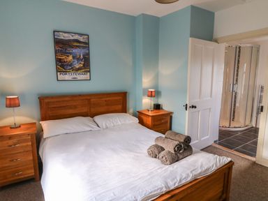 A bedroom with a wooden bed frame and bedside tables with lamps a poster on the wall and an open door leading to a bathroom at Rosies Cottage in Bushmills County Antrim