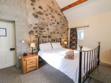 A bedroom with a metal bed frame white bedding stone wall wooden bedside tables and lamps at Rosies Cottage in Bushmills County Antrim