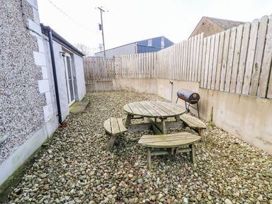An outdoor area with a round wooden picnic table and benches on a gravel surface at Rosies Cottage in Bushmills County Antrim