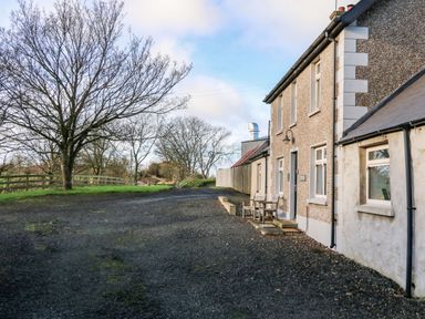 The exterior view of a house with gravel driveway and leafless trees at Rosies Cottage in Bushmills County Antrim