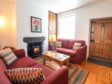A living room with two red sofas a wooden coffee table a fireplace and a wooden door at Siskin in Dinas Mawddwy near Dolgellau