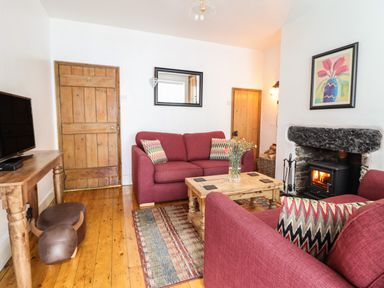 A living room with red sofas a wooden coffee table and a small fireplace at Siskin in Dinas Mawddwy near Dolgellau