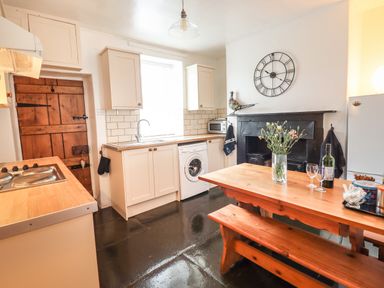 A kitchen with wooden table and bench a washing machine and a wooden door at Siskin in Dinas Mawddwy near Dolgellau