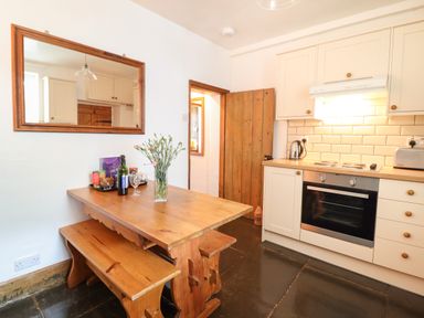 A kitchen with wooden dining table and benches glass vase with flowers and kitchen appliances at Siskin in Dinas Mawddwy near Dolgellau