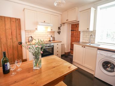 A kitchen with wooden table flowers wine bottle two glasses oven kettle toaster washing machine and wooden doors at Siskin in Dinas Mawddwy near Dolgellau