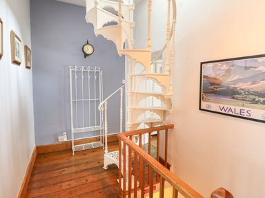 A hallway with a white spiral staircase wooden floor a wall clock and a framed Wales poster at Siskin in Dinas Mawddwy near Dolgellau