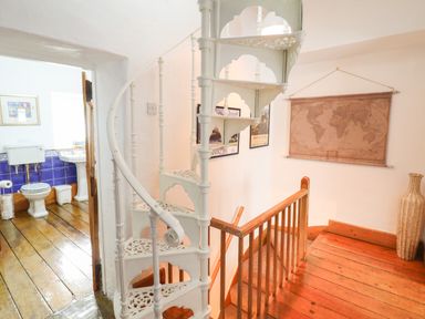 A wooden floor landing with a white spiral staircase a world map on the wall and a view into a bathroom at Siskin in Dinas Mawddwy near Dolgellau