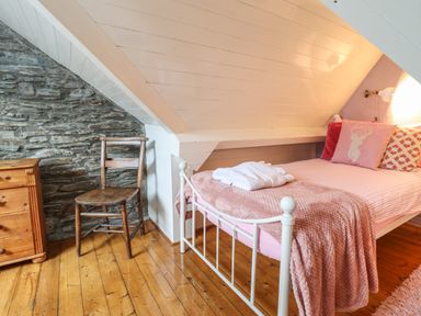 A small bedroom with a single bed with pink bedding wooden chair and a wooden chest of drawers at Siskin in Dinas Mawddwy near Dolgellau