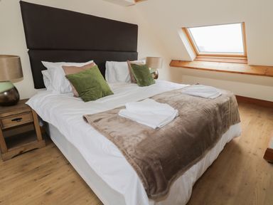 A bedroom with a large bed pillows a blanket two bedside tables with lamps and a skylight window at Dumbuie in Haltwhistle