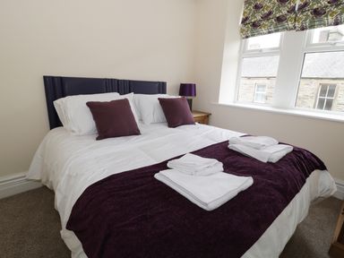 A bedroom with a bed folded towels pillows a lamp and windows at Dumbuie in Haltwhistle