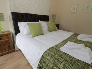 A bedroom with a double bed green pillows and lamps on wooden bedside tables at Dumbuie in Haltwhistle
