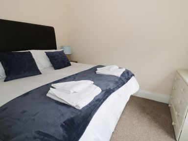 A bedroom with a bed with folded towels on a blanket and a white dresser at Dumbuie in Haltwhistle
