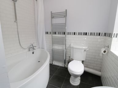 A bathroom with a bathtub a toilet a chrome towel rail and tiled walls at Dumbuie in Haltwhistle