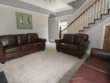 A sitting room with three brown leather sofas a painting of two hares on the wall and a staircase at Dumbuie in Haltwhistle