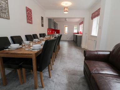 A dining area with a wooden table set with dishes and black chairs next to a kitchen with grey cabinets and red backsplash at Dumbuie in Haltwhistle