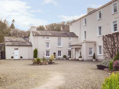 A large white building with multiple windows and a gravel driveway with potted plants at Rhydlandgoed in Stepaside near Saundersfoot