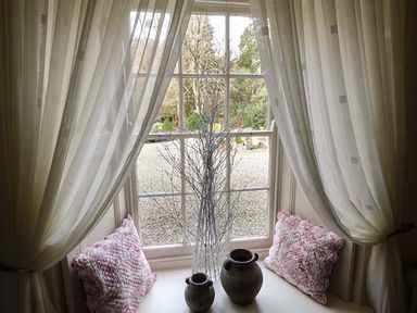 A window with sheer curtains and two cushions on the windowsill with two pottery vases and decorative branches at Rhydlandgoed Stepaside near Saundersfoot