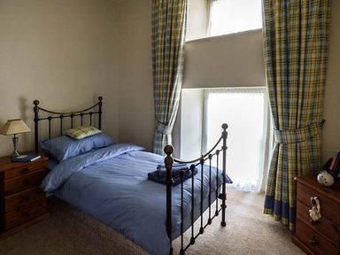 A bedroom with a metal bed frame blue bedding wooden nightstands and plaid curtains at Rhydlandgoed Stepaside near Saundersfoot