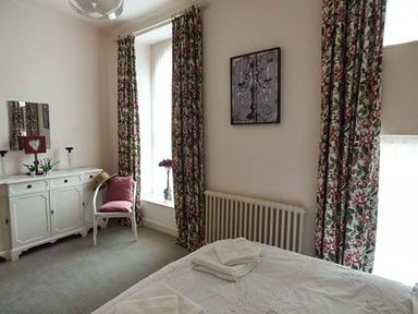 A bedroom with a bed folded towels a white dresser a chair and floral curtains at Rhydlandgoed in Stepaside near Saundersfoot