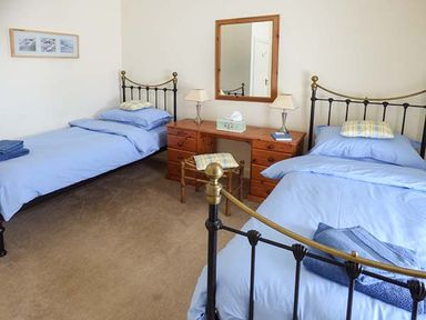 A bedroom with two single beds blue bedding a wooden dresser with lamps and a mirror at Rhydlandgoed in Stepaside near Saundersfoot