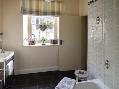 A bathroom with a sink a bathtub a small stool and a window with a striped blind at Rhydlandgoed Stepaside near Saundersfoot
