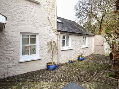 A courtyard with cobblestone floor blue plant pots white stone walls with windows and a wooden gate at Rhydlandgoed in Stepaside near Saundersfoot