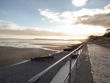 A beach with a concrete walkway and metal railing along the shore at Rhydlandgoed in Stepaside near Saundersfoot