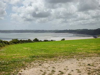 A grassy field overlooking a beach and the sea under a partly cloudy sky at Rhydlandgoed in Stepaside near Saundersfoot