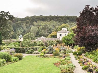 A garden with pathways shrubs and a white house in the background at Rhydlandgoed Stepaside near Saundersfoot