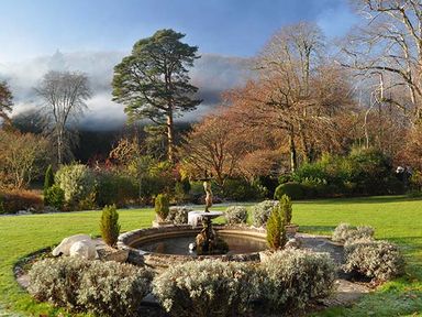 A circular stone water fountain surrounded by shrubs and trees in a garden at Rhydlandgoed Stepaside near Saundersfoot