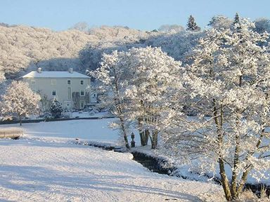 A snow-covered landscape with trees and a large house in the background at Rhydlandgoed in Stepaside near Saundersfoot