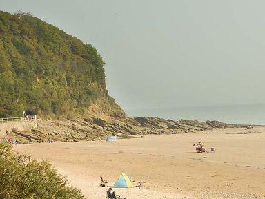 A beach with people sitting and small tents near a rocky hillside at Rhydlandgoed in Stepaside near Saundersfoot