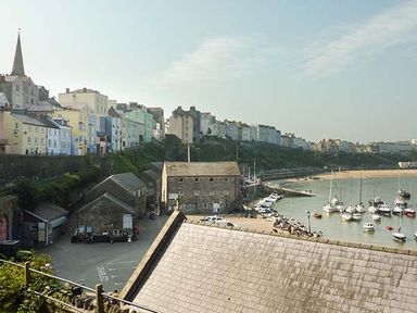 A coastal town with colorful buildings on a hill overlooking a marina with boats and a sandy beach at Rhydlandgoed in Stepaside near Saundersfoot
