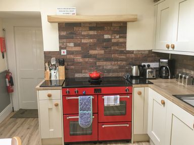 A kitchen with a red oven stove, utensils holder, kettle, toaster, coffee maker, and brick backsplash at Rhydlandgoed Stepaside near Saundersfoot